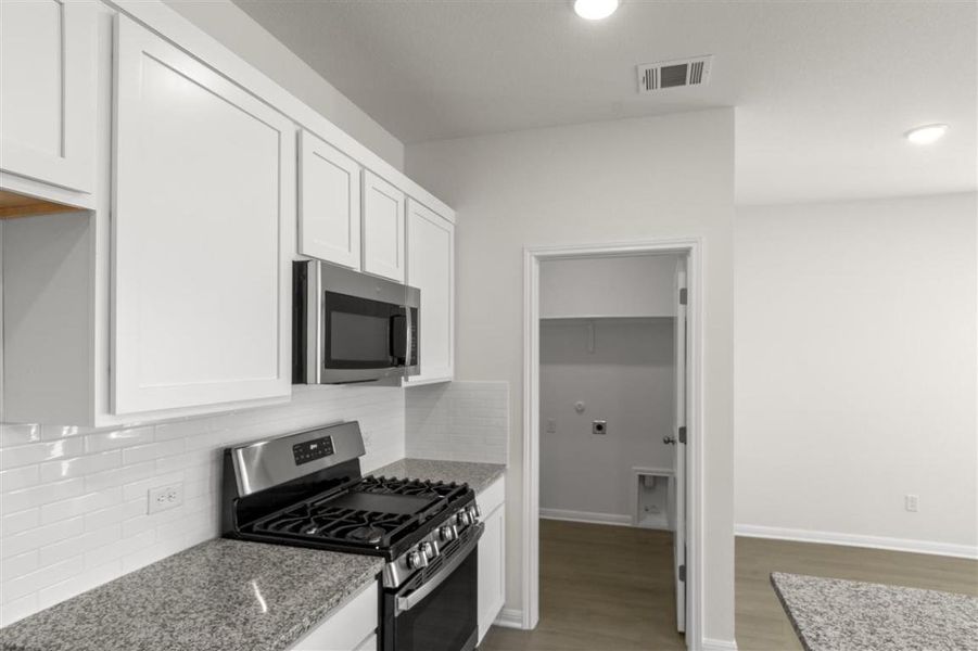 Kitchen with visible vents, light wood-style flooring, appliances with stainless steel finishes, white cabinetry, and light stone countertops
