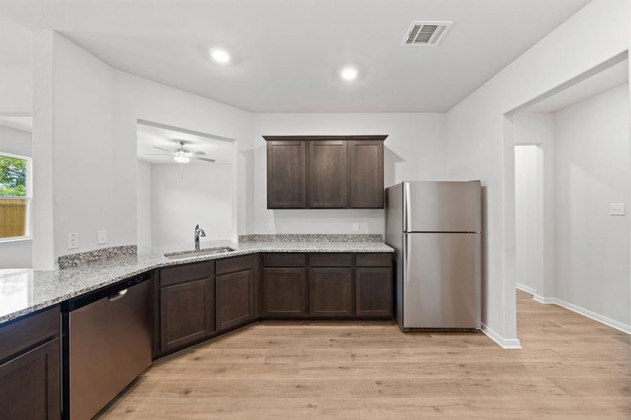 Kitchen with ceiling fan, sink, stainless steel appliances, light stone counters, and light wood-type flooring