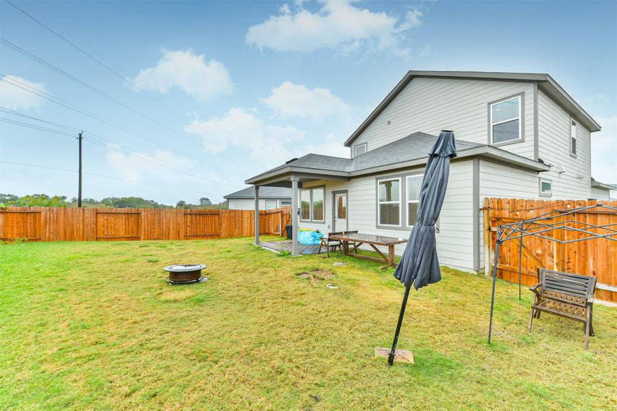 This backyard features a spacious lawn with a covered patio area perfect for outdoor dining and relaxation. The exterior of the house is modern with multiple windows for natural light. ** All extra items will be removed by the landlord**