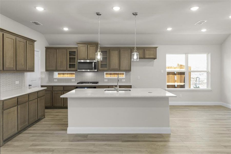 Kitchen with hanging light fixtures, tasteful backsplash, a kitchen island with sink, appliances with stainless steel finishes, and sink