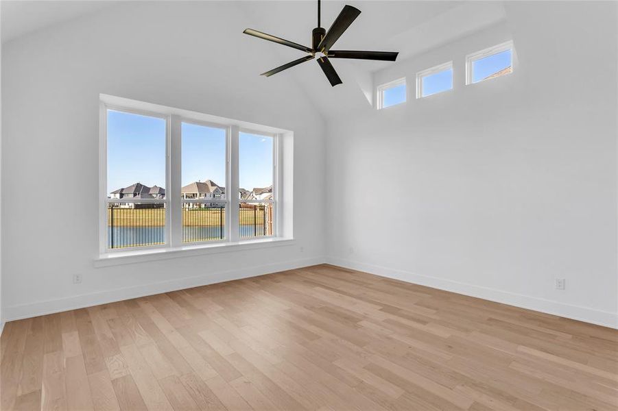 Empty room with a residential view, light wood finished floors, high vaulted ceiling, ceiling fan, and a water view
