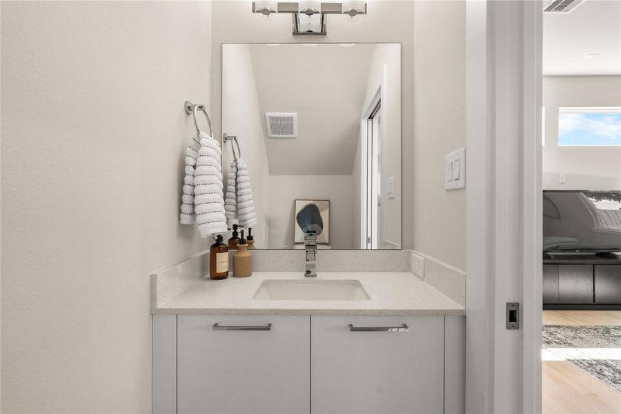 Elegant powder bath featuring a quartz countertop, sleek cabinetry & a large mirror that adds depth & sophistication to the space.