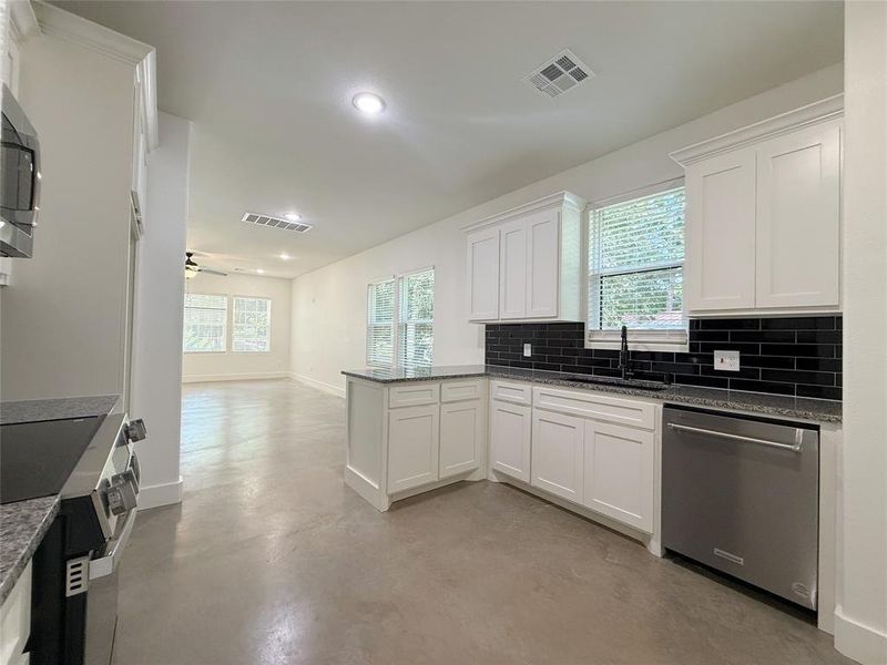 Kitchen with finished concrete flooring, stainless steel appliances, a peninsula, tasteful backsplash, and white cabinets