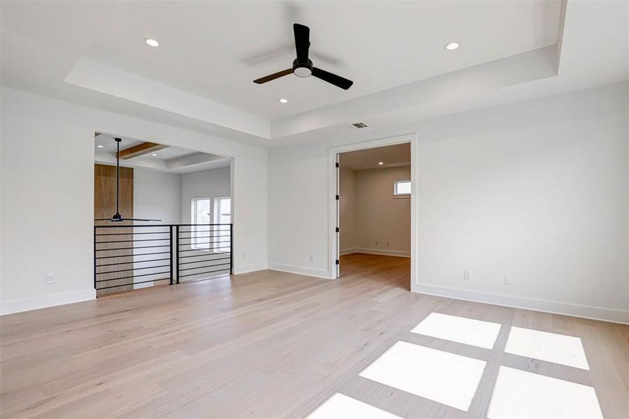 Spare room with light hardwood / wood-style flooring, ceiling fan, and a tray ceiling