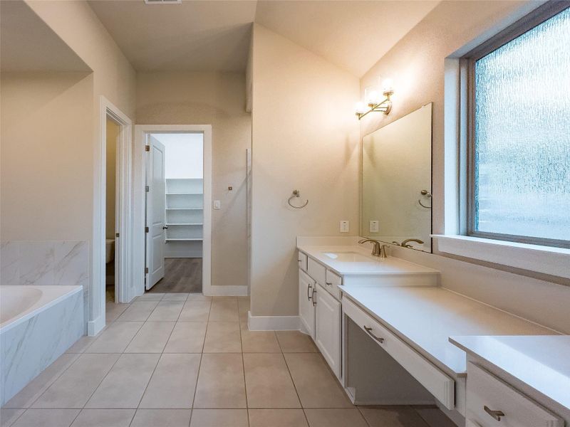 Bathroom featuring vanity, light tile patterned flooring, a walk in closet, and a tub with marble appearance Bathroom featuring vanity, light tile patterned flooring, a walk in closet, and a tub with marble appearance