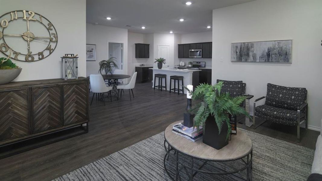 Open-concept living area featuring wood-finish flooring, recessed lighting, and a kitchen with dark cabinetry, stainless steel appliances, and a breakfast bar Open-concept living area featuring wood-finish flooring, recessed lighting, and a kitchen with dark cabinetry, stainless steel appliances, and a breakfast bar