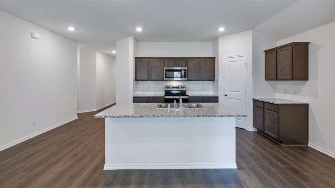 Kitchen featuring dark wood finish cabinets, decorative backsplash, stainless steel appliances, light stone counters, and recessed lighting