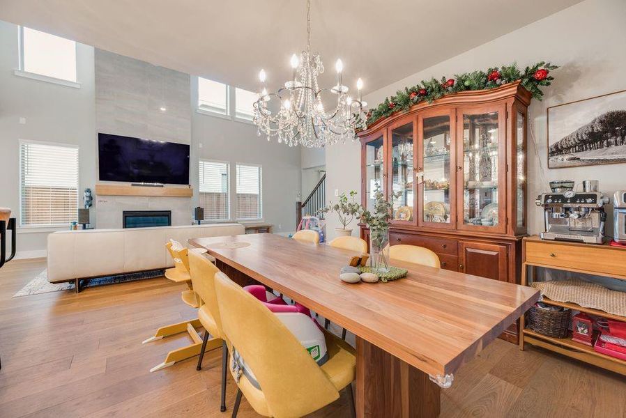 Dining space featuring a high ceiling, light wood-style flooring, a fireplace, and hanging lights
