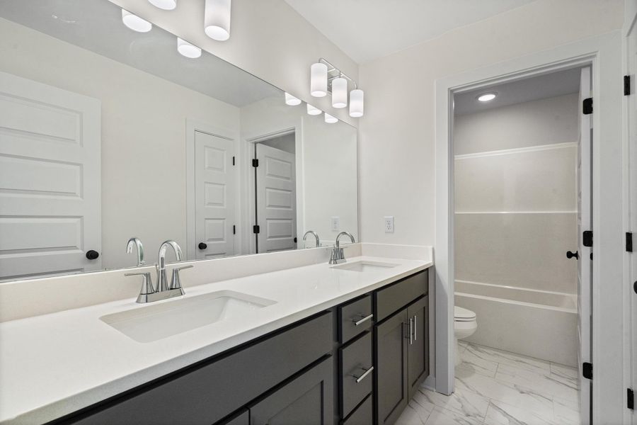 Bathroom featuring a dual-sink vanity with a light-colored countertop, dark cabinetry, and chrome fixtures Bathroom featuring a dual-sink vanity with a light-colored countertop, dark cabinetry, and chrome fixtures