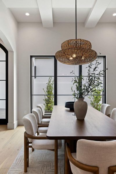 Dining area featuring a natural woven pendant light, coffered ceiling, light wood-finish flooring, and black-framed windows