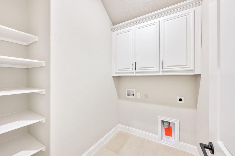 Laundry room with white upper cabinets, open shelving, and washer and dryer hookups on white walls Laundry room with white upper cabinets, open shelving, and washer and dryer hookups on white walls