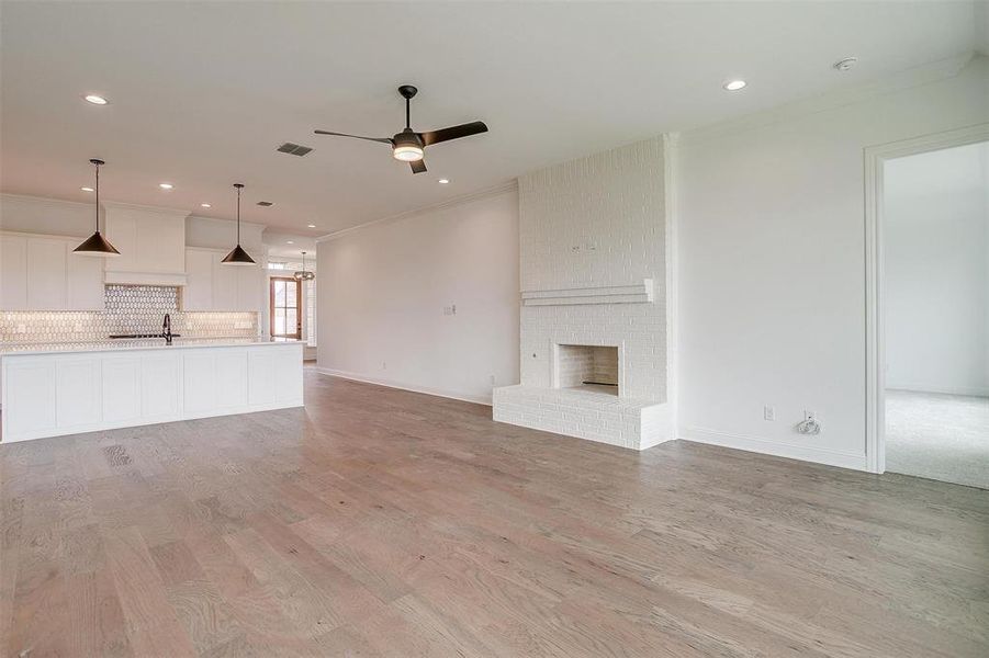 Unfurnished living room with ornamental molding, a brick fireplace, ceiling fan, and light hardwood / wood-style flooring