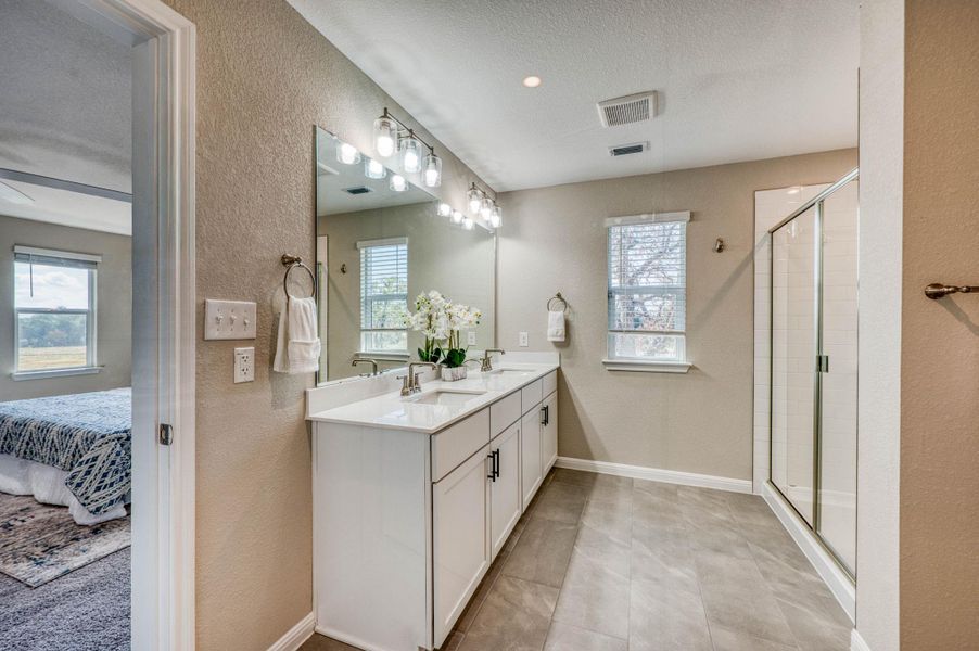 Double vanities and a glass-enclosed shower highlight this tiled primary bathroom. Double vanities and a glass-enclosed shower highlight this tiled primary bathroom.