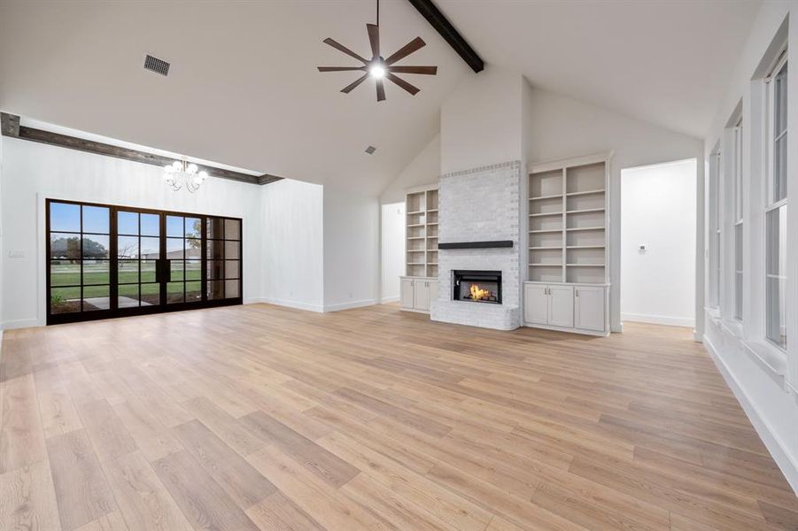 Unfurnished living room featuring a brick fireplace, high vaulted ceiling, light wood-style floors, beamed ceiling, and a ceiling fan