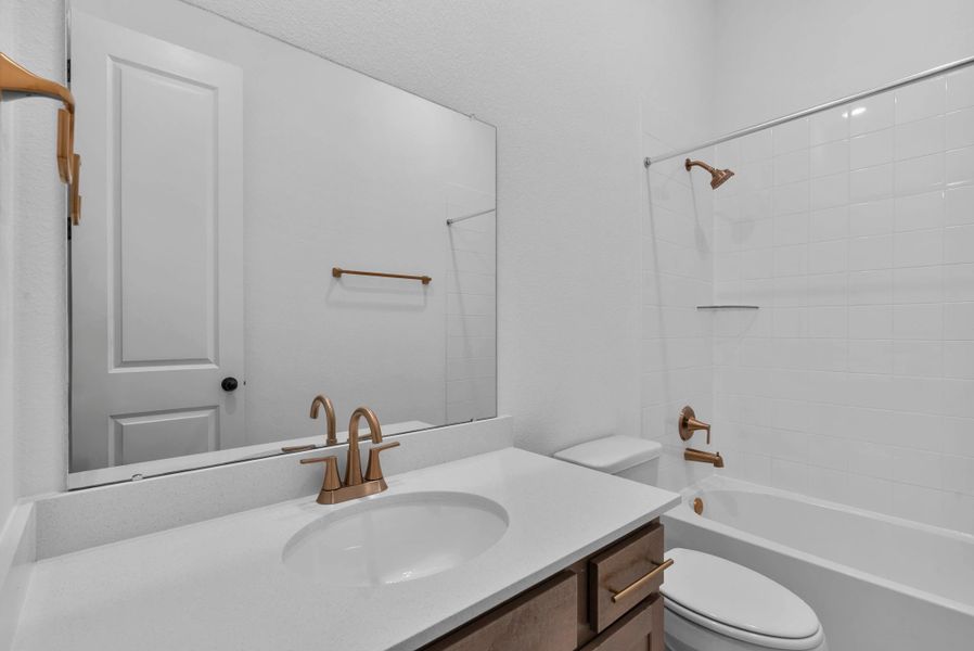 Stylish secondary bath featuring the AW Collection Laguna with stained cabinetry and light countertops with brass fixtures and a shower/tub combo.