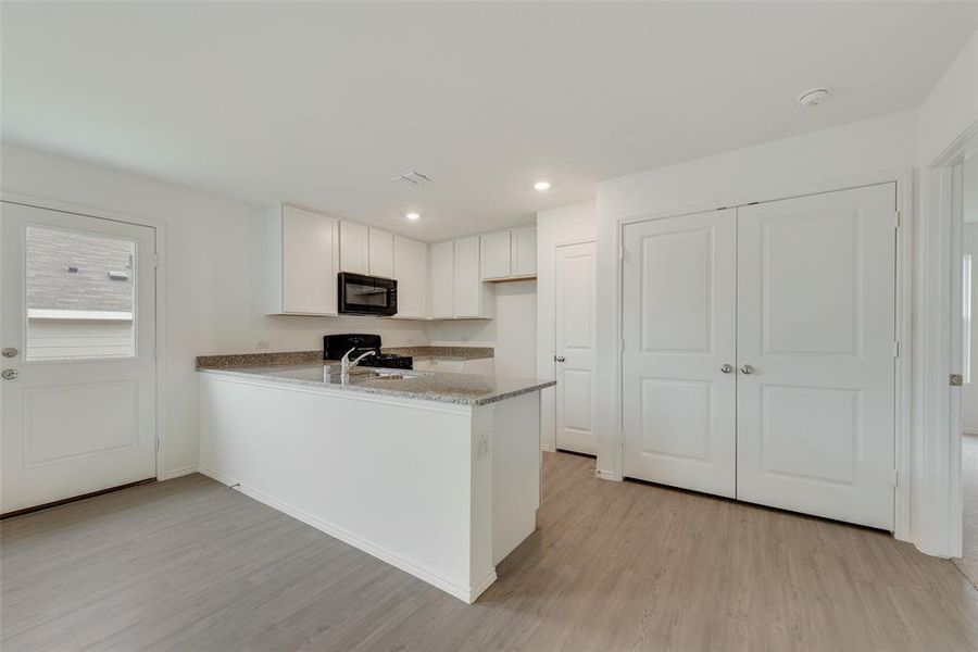 Kitchen featuring black appliances, white cabinets, light stone counters, kitchen peninsula, and light wood-type flooring