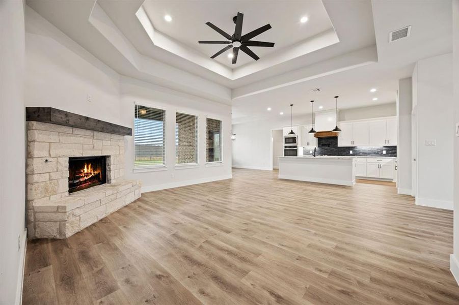 Unfurnished living room featuring light wood finished floors, visible vents, ceiling fan, a tray ceiling, and a fireplace