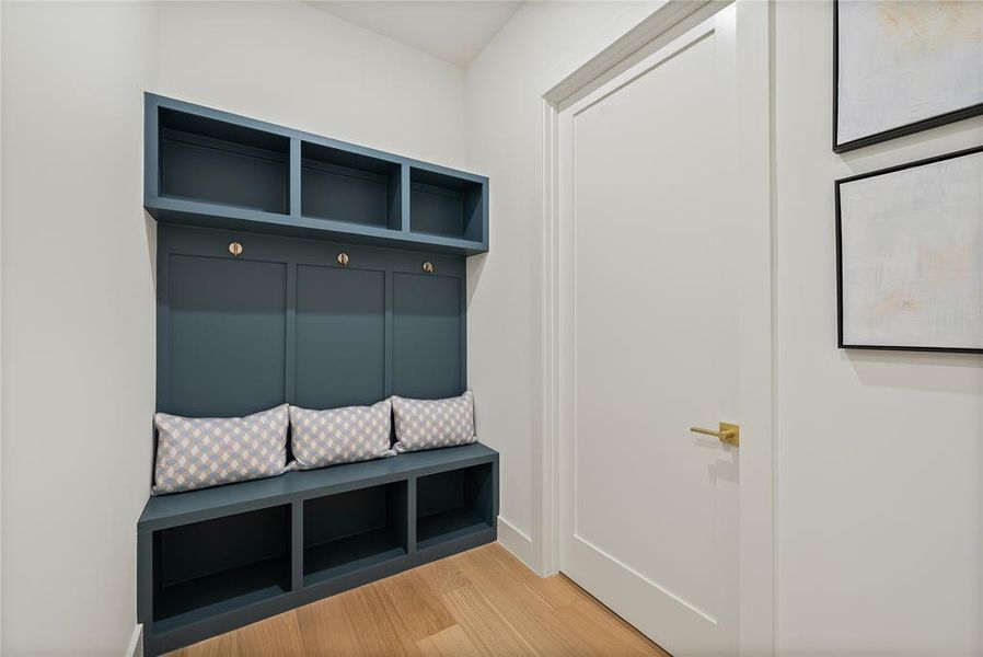 Entryway featuring built-in storage with shelves, hooks, and a bench, alongside a white door with a gold-toned handle, and light wood flooring