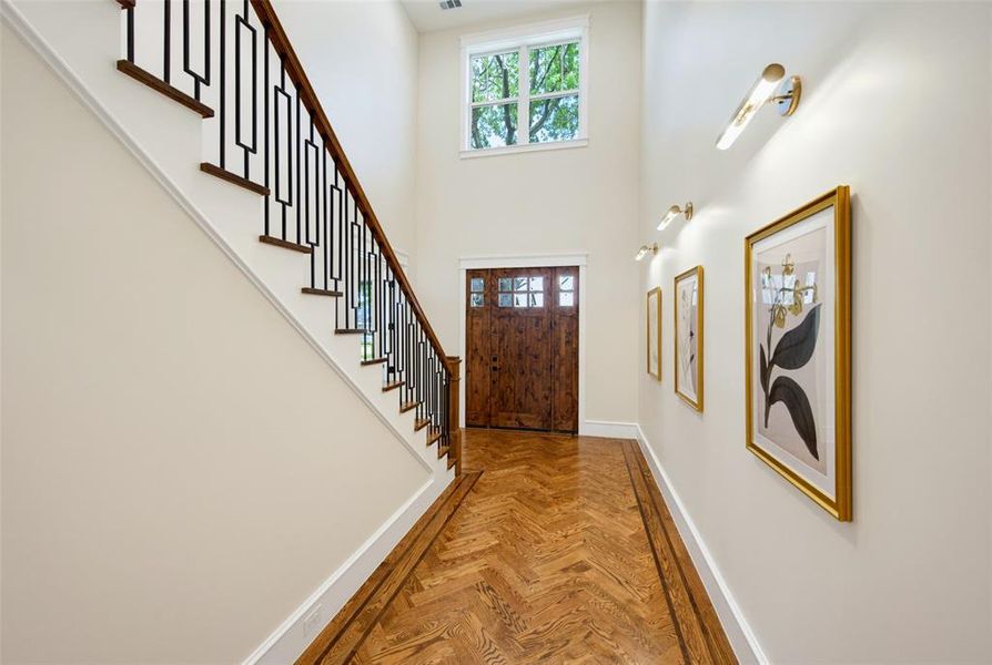 Entryway featuring high ceilings, wood-finish herringbone flooring, a decorative wood front door, and a staircase with dark wood treads and a black metal railing