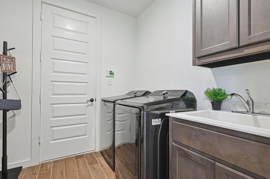 Clothes washing area with washer and dryer, hardwood / wood-style floors, sink, and cabinets