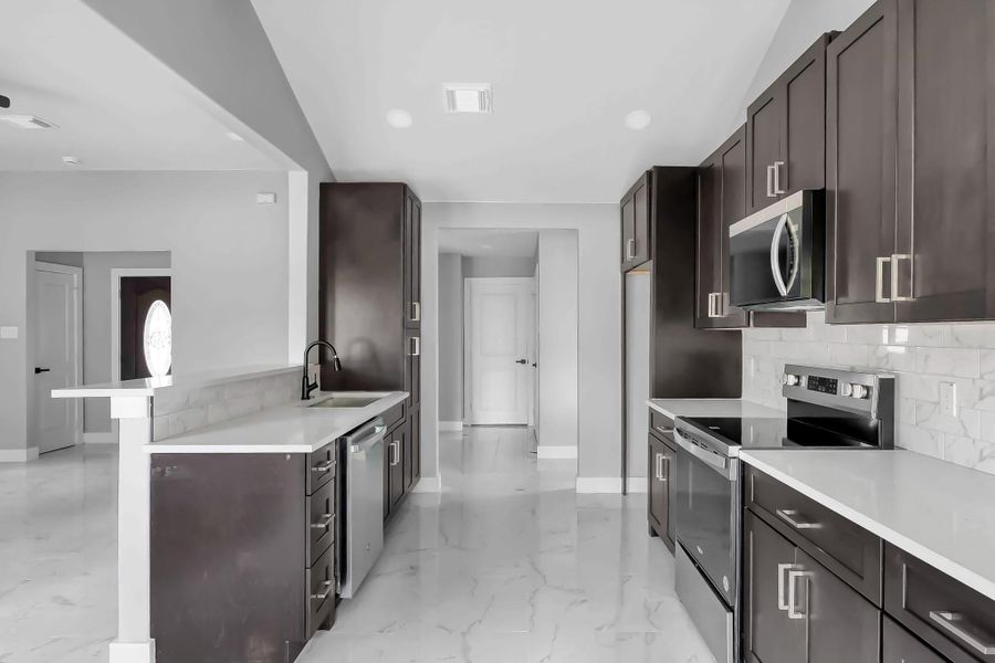 This modern kitchen features sleek dark cabinets, stainless steel appliances, and light countertops. It offers ample storage and workspace, with marble-like flooring and a bright, open layout.