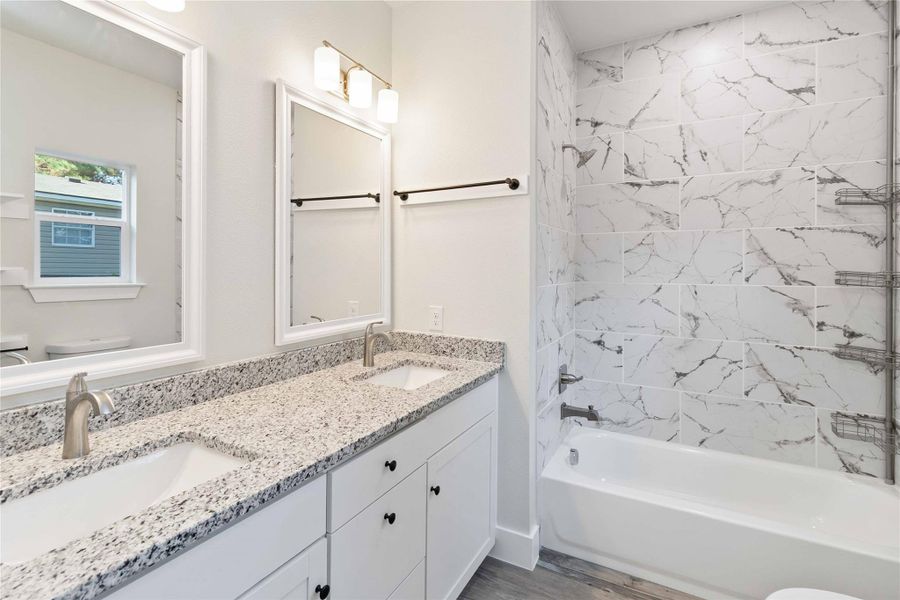 Full bath with shower / bath combination, double vanity, and light wood-style floors