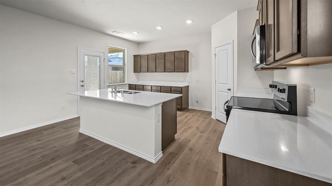 Spacious kitchen featuring an island, light wood-finish flooring, white countertops, dark wood cabinetry, and stainless steel appliances