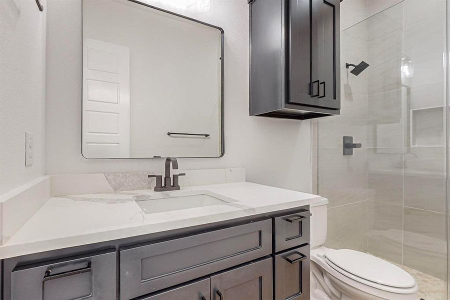 Bathroom featuring tiled shower, vanity, and toilet