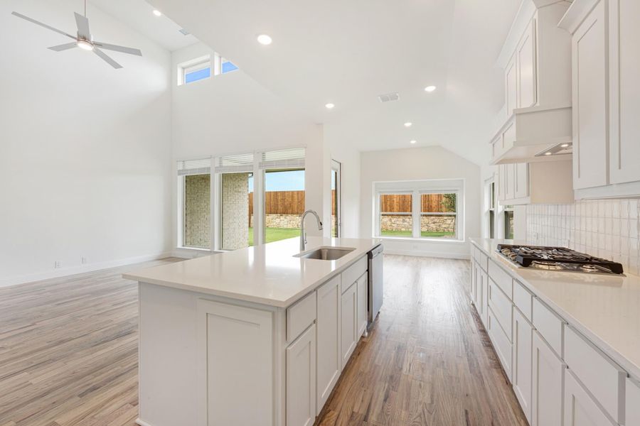 Open kitchen with white cabinets, center island with sink, quartz countertops, and hardwood floors under vaulted ceiling Open kitchen with white cabinets, center island with sink, quartz countertops, and hardwood floors under vaulted ceiling