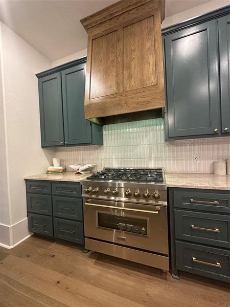 Gourmet kitchen featuring a stainless steel professional range, wood-finish range hood, blue-gray cabinetry, light-toned countertops, and vertical subway tile backsplash