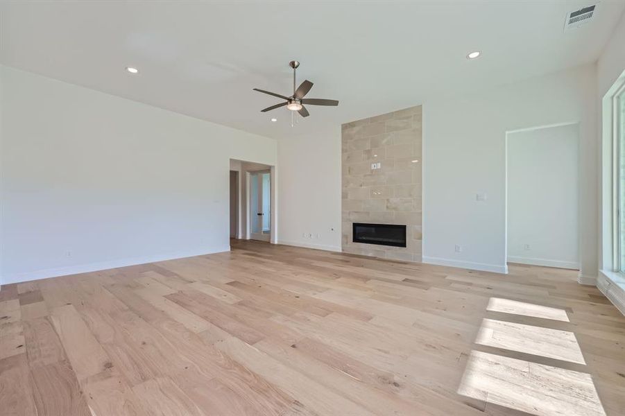 Unfurnished living room featuring light hardwood / wood-style flooring, a tiled fireplace, and ceiling fan