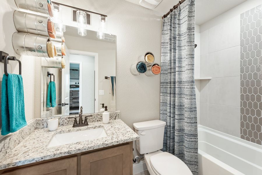 Bathroom with granite vanity, wood cabinets, toilet, and tub with hexagon tile and gray shower curtain Bathroom with granite vanity, wood cabinets, toilet, and tub with hexagon tile and gray shower curtain