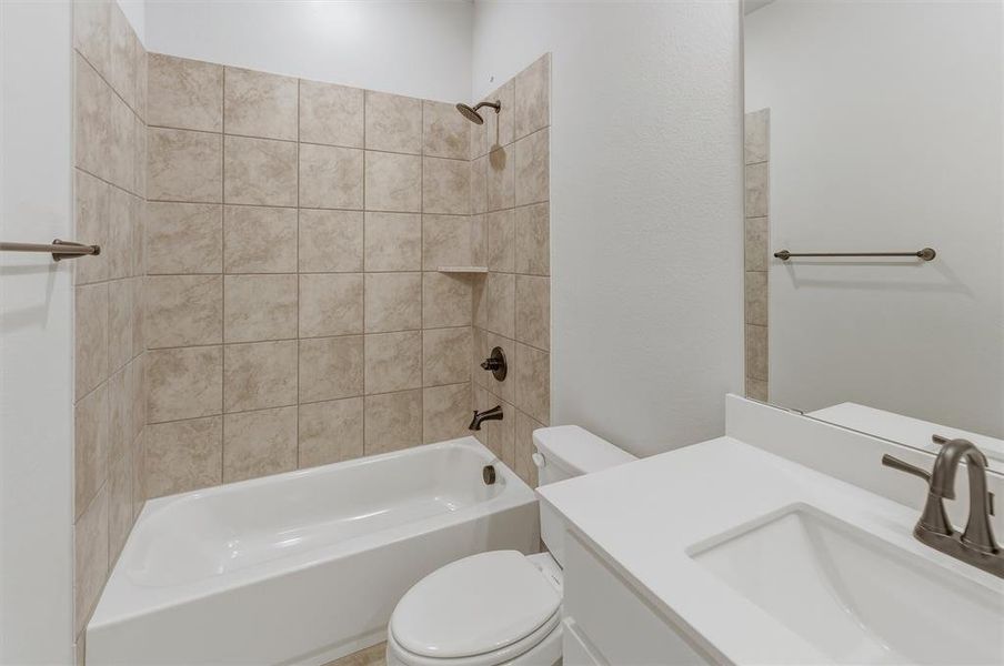 Bathroom featuring a white bathtub, ceramic tile surround, built-in shower niche, toilet, and a vanity with an integrated sink and mirror