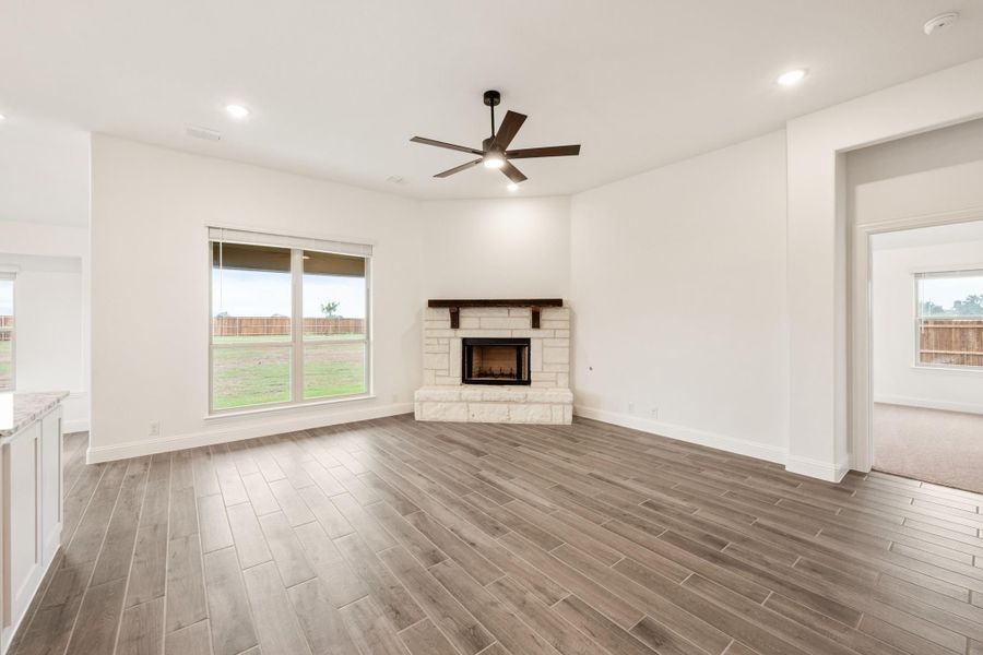 Open living room with wood-look tile floors, stone fireplace, and ceiling fan