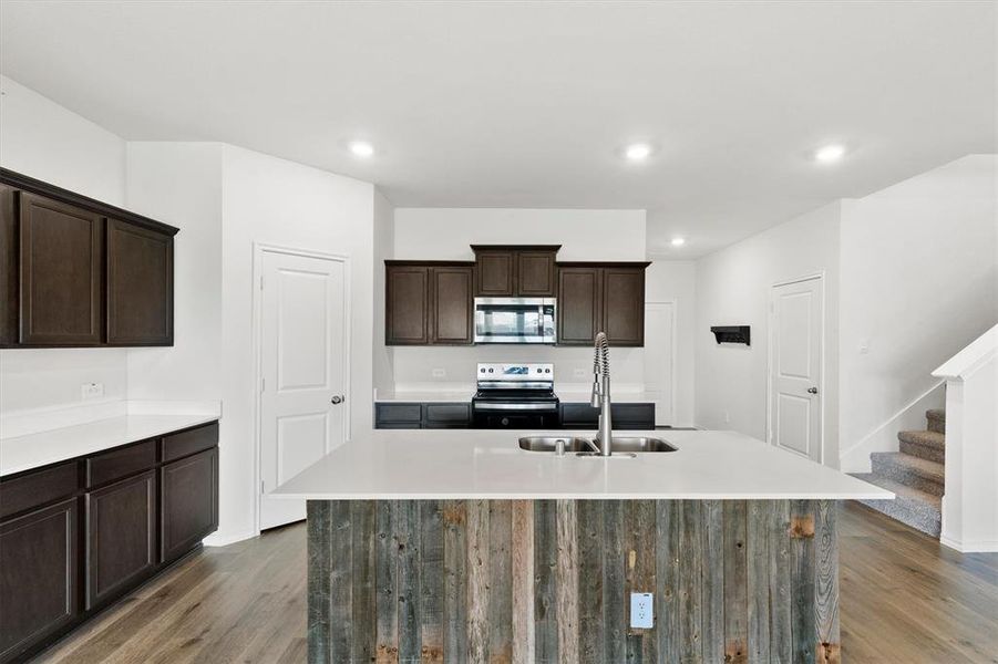 Kitchen island featuring a wood-finish facade, integrated stainless steel sink, and a high-arc faucet