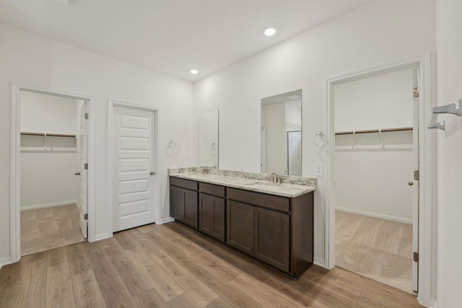 Bathroom with a walk in closet, double vanity, light wood finished floors, and recessed lighting