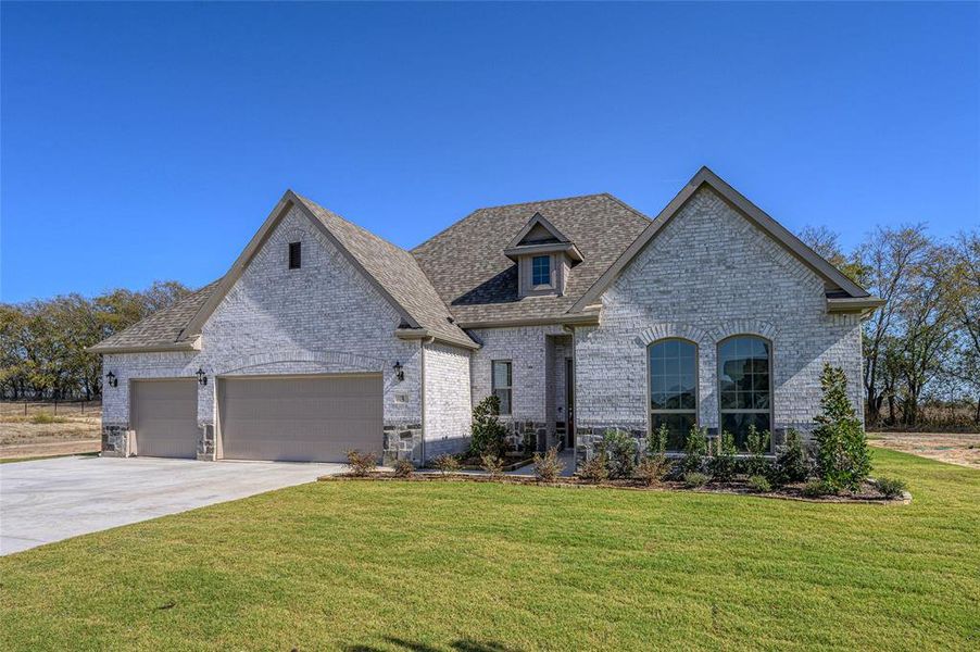 French country style house featuring brick siding, a front lawn, concrete driveway, a garage, and a shingled roof French country style house featuring brick siding, a front lawn, concrete driveway, a garage, and a shingled roof