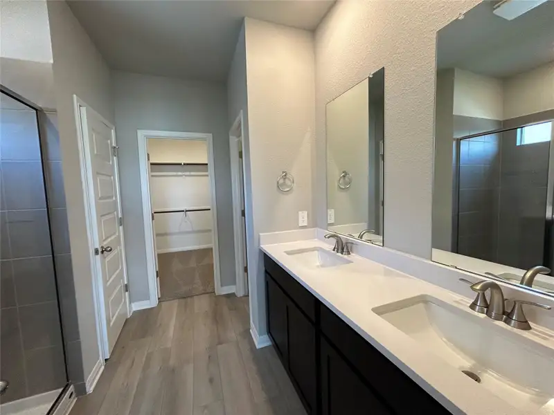 Full bathroom with a shower stall, wood finished floors, double vanity, and a spacious closet