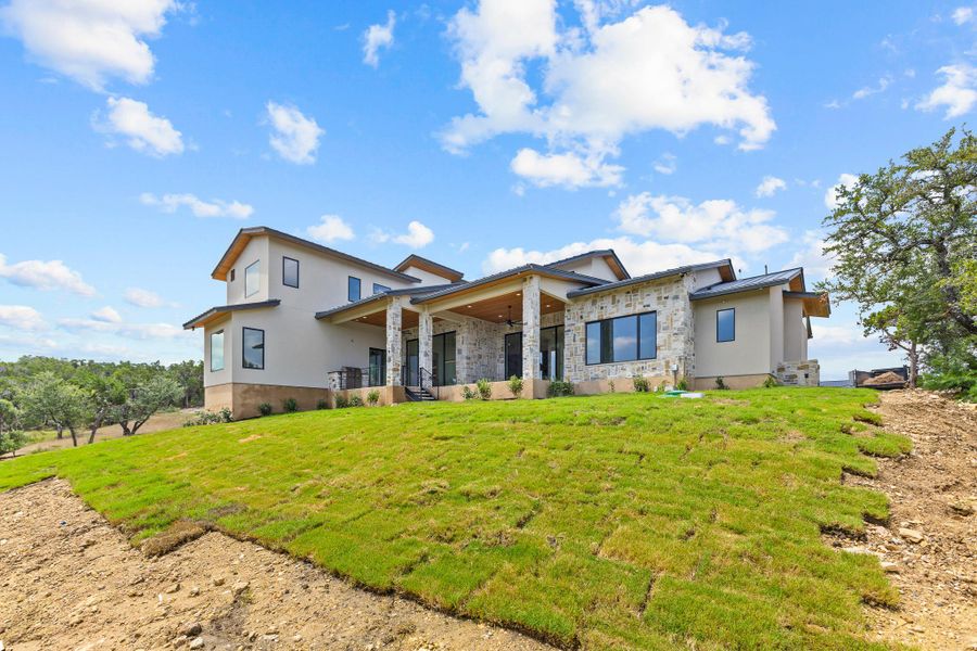 A striking modern residence with a blend of stucco and stone accents, complemented by a covered patio and expansive, newly laid lawn. A striking modern residence with a blend of stucco and stone accents, complemented by a covered patio and expansive, newly laid lawn.