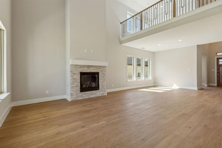 Unfurnished living room with a fireplace, light wood-type flooring, and a towering ceiling