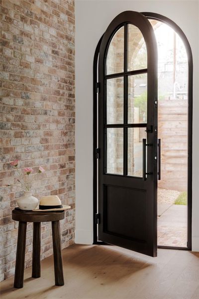 Foyer with light wood-type flooring, brick wall, and arched walkways