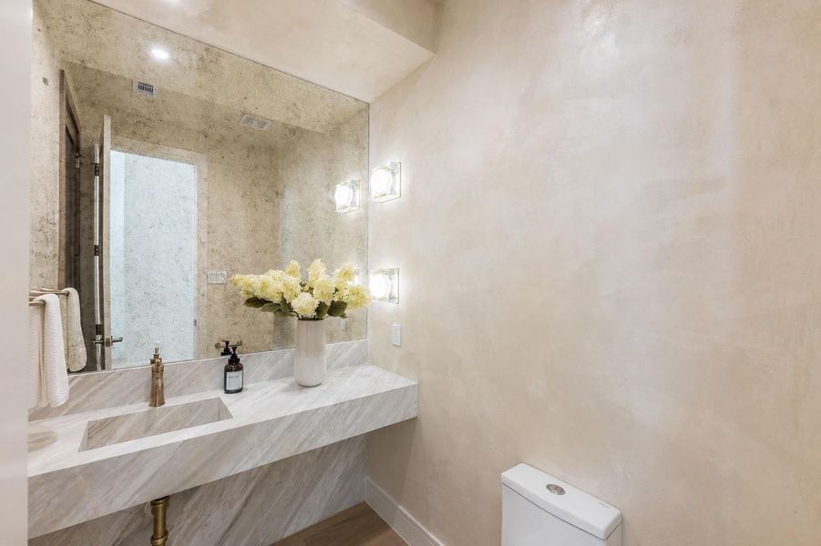 A jewel-box powder bath that makes a lasting impression, showcasing a striking waterfall marble vanity with dramatic veining and warm brass fixtures. Sculptural wall sconces cast a soft glow, creating an intimate space where every detail feels intentionally elevated.