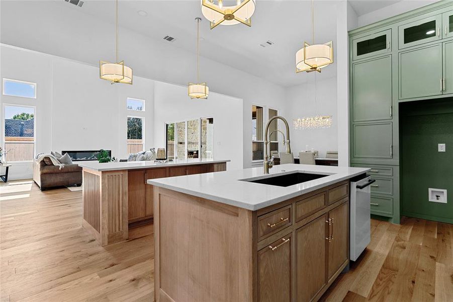 Kitchen with open floor plan, hanging light fixtures, light stone countertops, light wood finished floors, and glass insert cabinets Kitchen with open floor plan, hanging light fixtures, light stone countertops, light wood finished floors, and glass insert cabinets