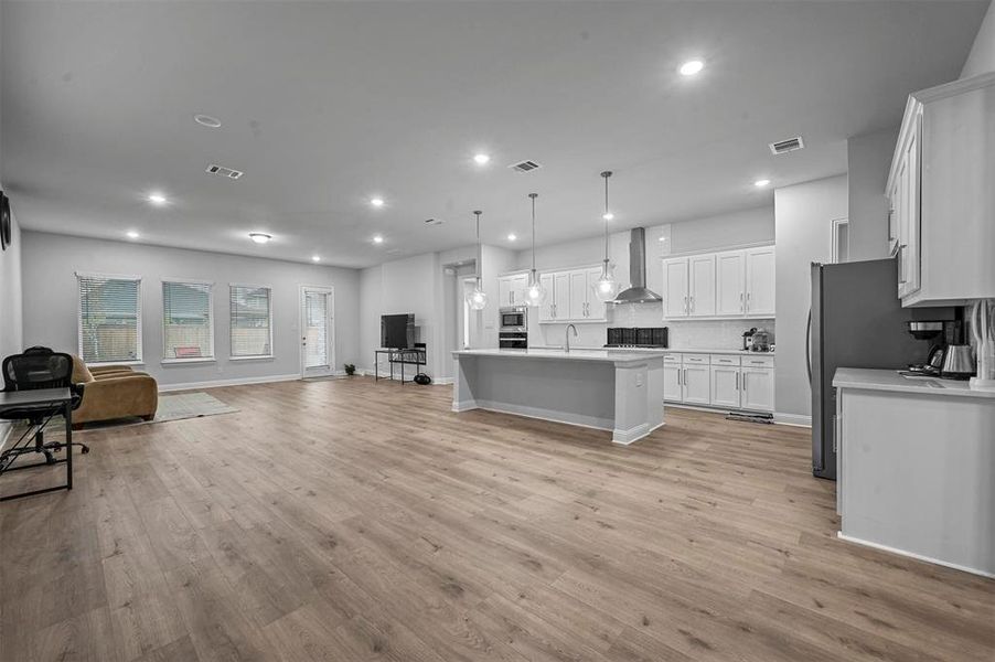 Kitchen with open floor plan, white cabinetry, an island with sink, decorative light fixtures, and light wood floors