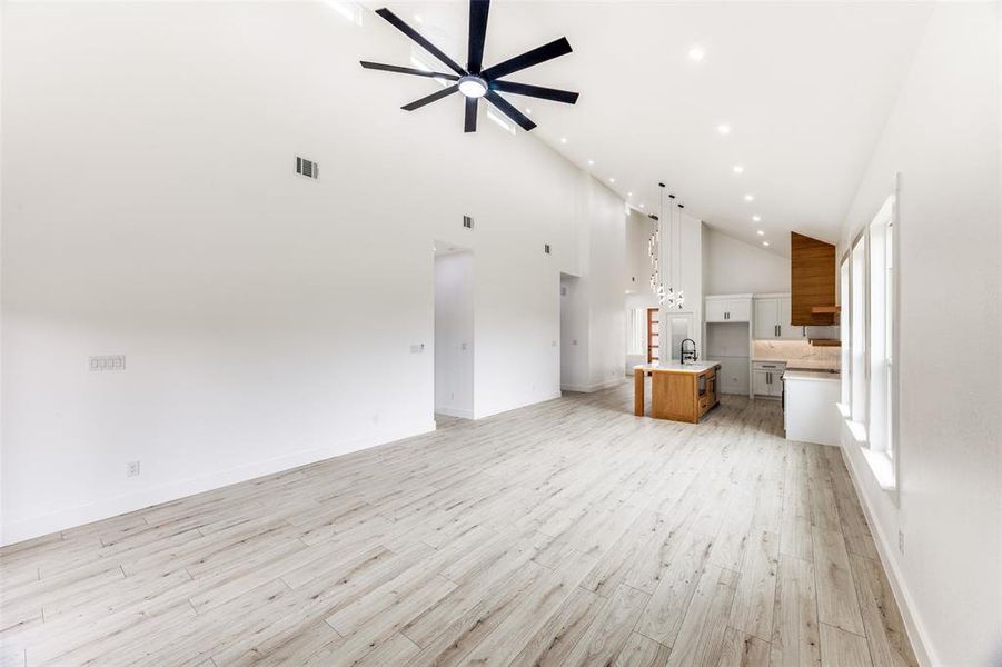 Unfurnished living room with high vaulted ceiling, light wood finished floors, recessed lighting, and ceiling fan Unfurnished living room with high vaulted ceiling, light wood finished floors, recessed lighting, and ceiling fan