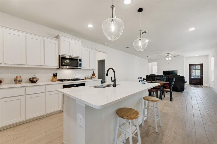 Kitchen featuring light wood finished floors, white cabinetry, decorative light fixtures, tasteful backsplash, and open floor plan Kitchen featuring light wood finished floors, white cabinetry, decorative light fixtures, tasteful backsplash, and open floor plan
