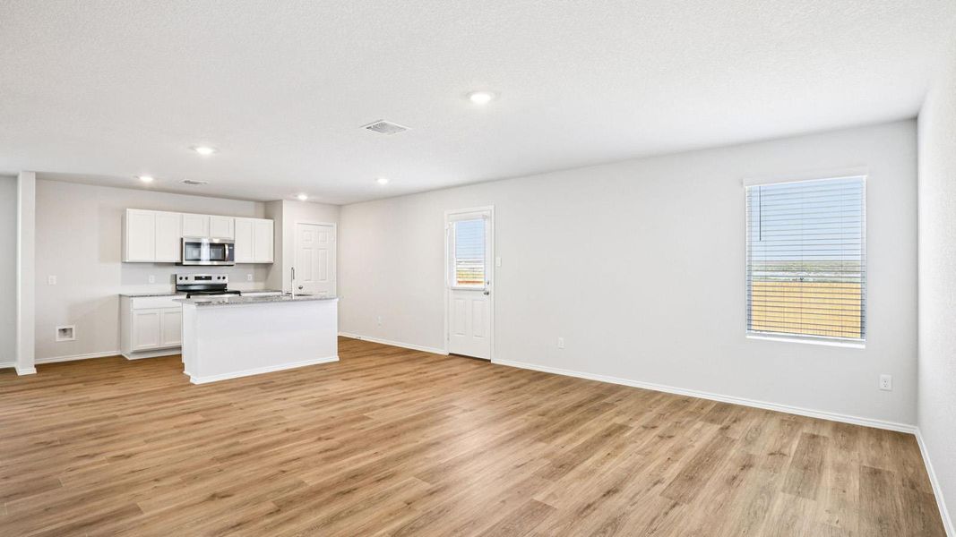 Open-concept living area featuring wood-finish flooring, recessed lighting, and a kitchen with white cabinetry, stainless steel appliances, and a central island with a countertop