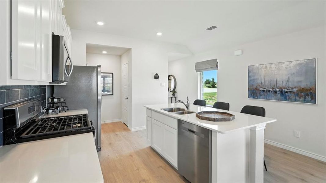 Kitchen featuring white cabinetry, a kitchen bar, backsplash, stainless steel appliances, and a kitchen island with sink
