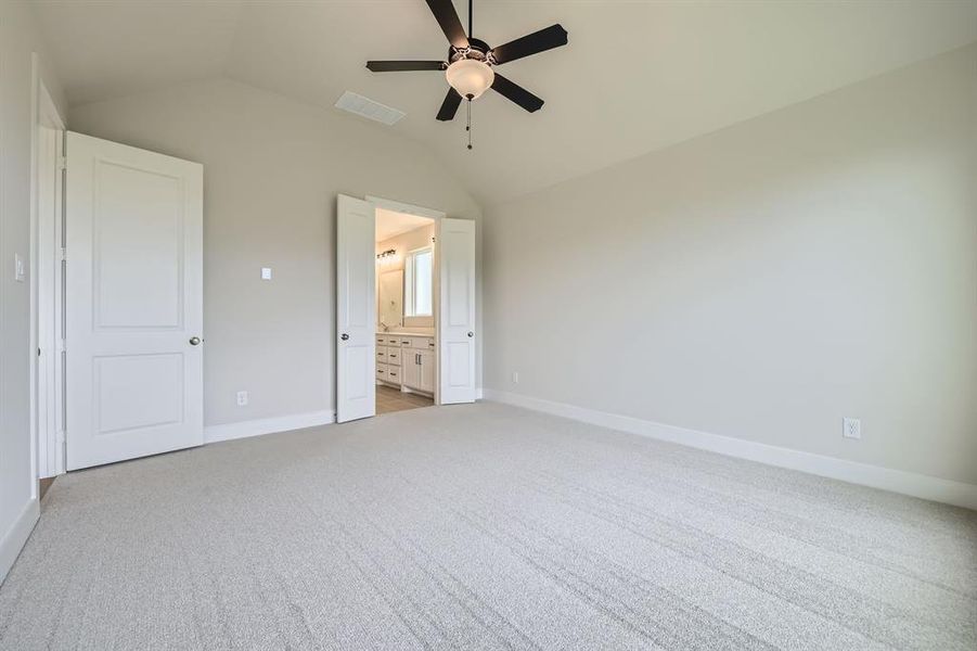 Unfurnished bedroom with lofted ceiling, light colored carpet, ensuite bathroom, and ceiling fan