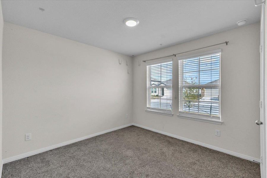 This room features white walls, carpet flooring, and two windows with blinds